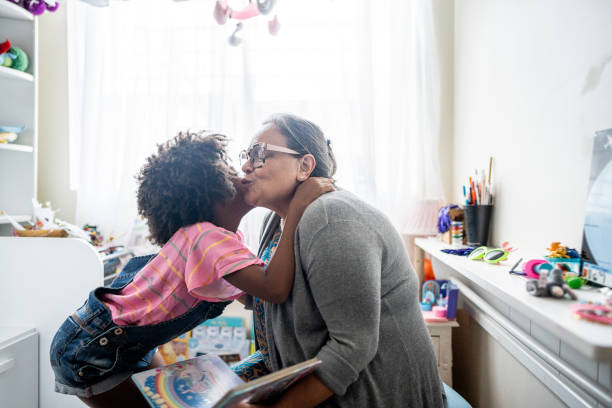 девочка целует бабушку в щеку в гостиной дома - grandparent family reading inside of стоковые фото и изображения