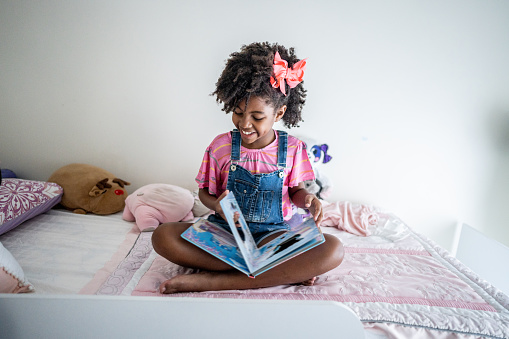 Girl child reading a book on her bedroom at home