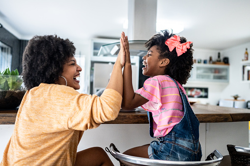 Young mother doing high-five with her daugther at home