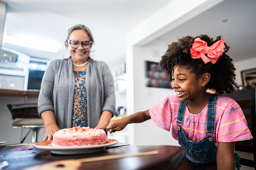 Girl child cutting a piece birthday cake with her family at home