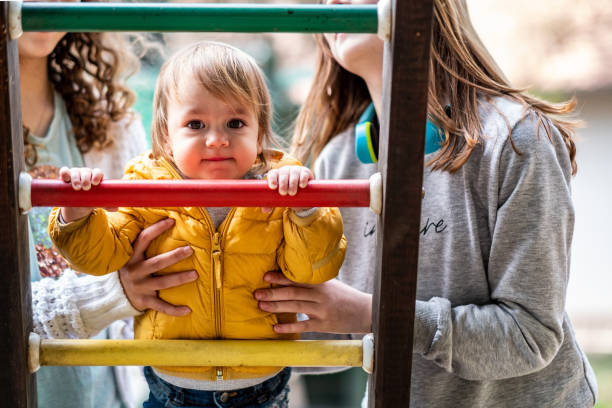 teenage girls with a baby on the playground teenage girls help the baby to climb on the play cognitive skills in babies stock pictures, royalty-free photos & images