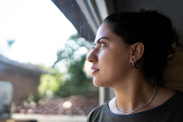 istock Young woman contemplating while looking through the window at home 1490772021