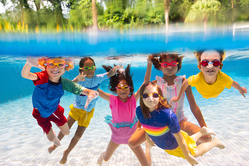 Group of kids jump into swimming pool. Summer water fun. Children play in outdoor pool. Summer family vacation with young kid. Holiday in tropical resort. Travel with child.