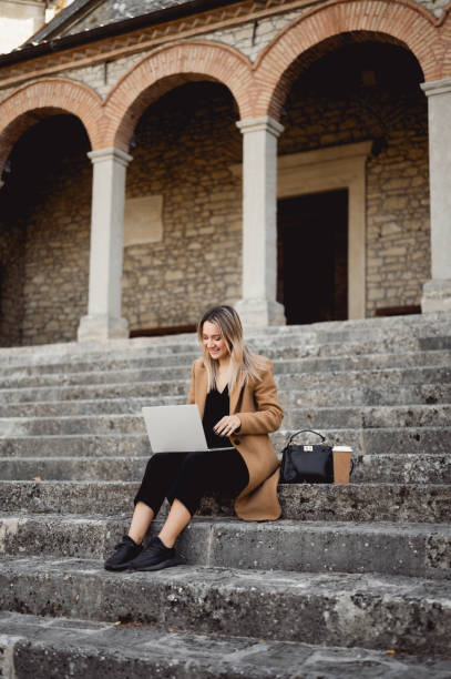 istock Young pretty woman working on laptop outdoors while sitting on a stairs. 1490781605