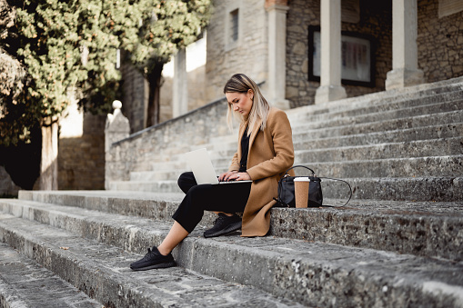 side view of a young woman studying outdoors on a stairs of University campus.