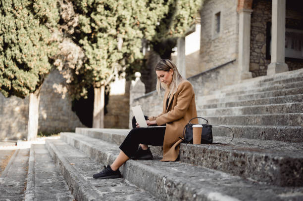 istock young woman sitting on a stairs outdoors and working on laptop. 1490781846