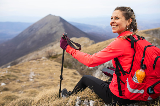 A happy woman hiker is taking a break to enjoy the view of the mountains