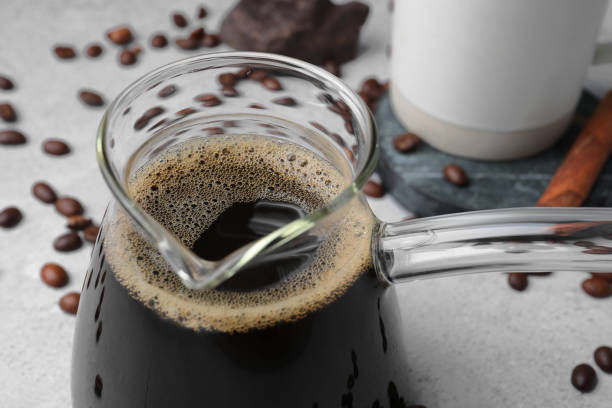 Turkish coffee in glass cezve and beans on light grey table, closeup