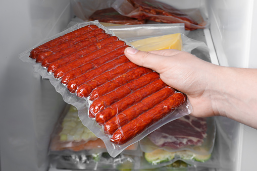 Woman putting vacuum bag with sausages into fridge, closeup. Food storage