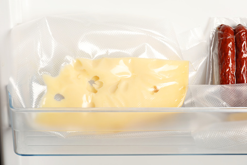 Vacuum bags with cheese and sausages in fridge, closeup. Food storage