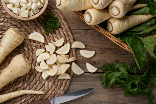 Whole and cut parsnips on wooden table, flat lay