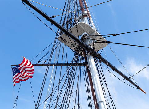 Waving American flag flying from the mast of a old square rigger sailing ship.