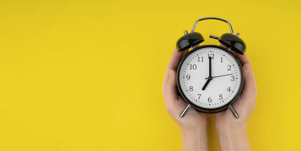 istock Woman's hands holding a black alarm clock on a yellow background 1490785300