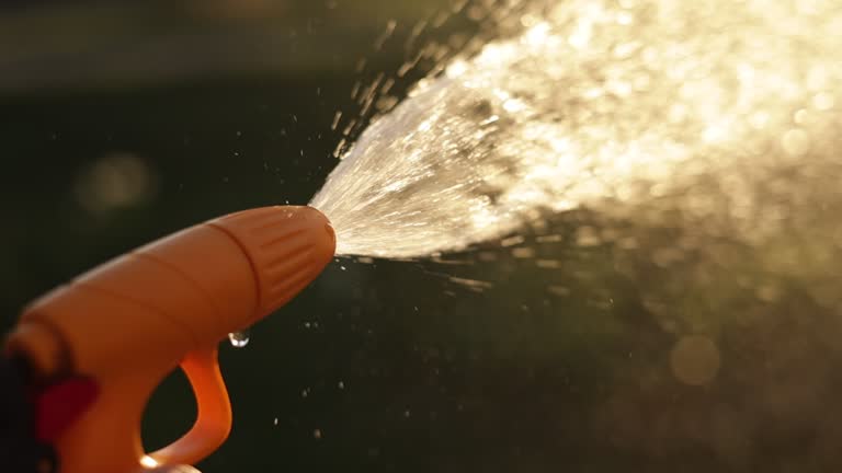 Close up hose nozzle spraying water in sunlight. Home gardening care concept on summertime with watering, sprinkler. Garden equipment. Eco-friendly farm lifestyle. Slow motion with blurred effect.