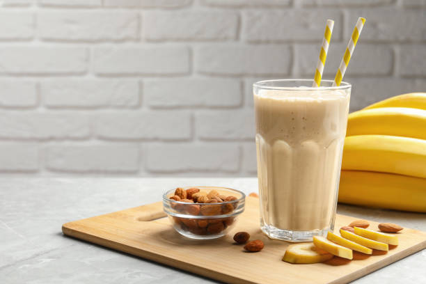 istock Banana smoothie in glass and nuts on light grey marble table against white brick wall. Space for text 1490791574