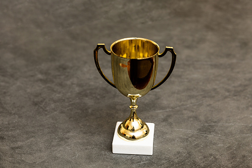 Simply design winner or champion gold trophy cup on concrete stone grey background. Victory first place of competition. Winning or success concept. Top view copy space