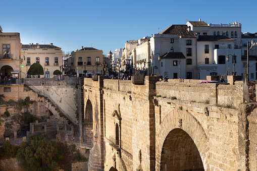 Ronda, Andalusia, Spain - March 15, 2023: The famous bridge with arched vaults between the rocks of the gorge on a sunny day. Landmark of the city