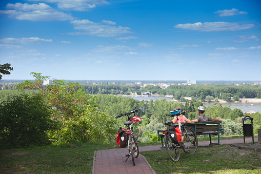 Picture of two persons, man and woman, a couple, doing bicycle touring in Ilok, in the Croatia slavonia, with their bikes. Bicycle touring is the taking of self-contained cycling trips for pleasure, adventure or autonomy rather than sport, commuting or exercise. Bicycle touring can range from single-day trips to extended travels spanning weeks or months. Tours may be planned by the participant or organized by a tourism business, local club or organization, or a charity as a fund-raising venture.