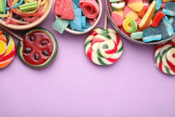 istock Many different jelly candies and lollipops on lilac background, flat lay. Space for text 1490797858