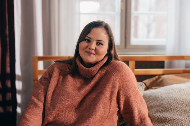 Portrait of a Beautiful Plus Size Woman Sitting in her Bed Room, Looking at Camera stock photo