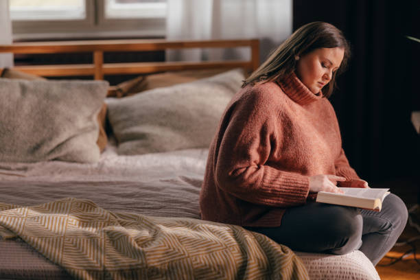 istock Beautiful Plus Size Woman Sitting on her Bed and Reading an Exciting Novel 1490798813