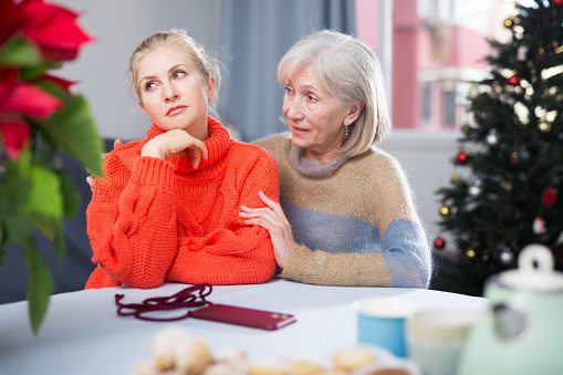 Mature woman gently hugged her adult, somewhat upset daughter, who came to visit her before Christmas