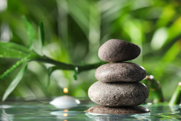 istock Stacked stones and burning candle with bamboo stem on water surface against blurred green leaves, closeup 1490803591