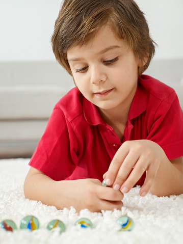Boy lying on carpet floor playing marbles.