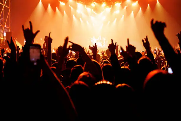 Photo of People with raised hands at a music concert. Fans in concert hall.