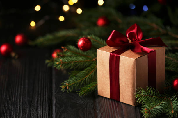 istock Beautiful gift box, fir tree branches and Christmas decor on wooden table against blurred festive lights, space for text 1490813769