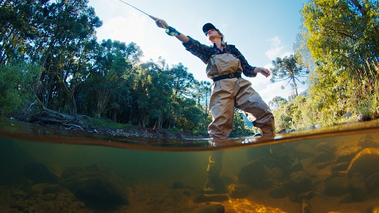 Mujer pescadora en el río. La mujer se para en el agua en zancudas y lanza la línea. Mujer pescando en el río photo