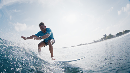 Surfer rides the wave. Young man surfs the ocean wave in the Maldives and looks into the camera