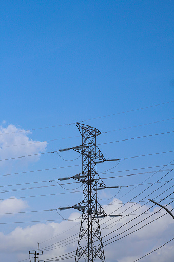 electric towers and cables that stretch against a bright blue sky and cloudy background