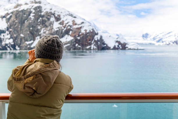 a young woman with binoculars views the snow covered mountains and glaciers from a cruise ship balcony at glacier bay national park and reserve, alaska usa. - ice cold glacier blue imagens e fotografias de stock