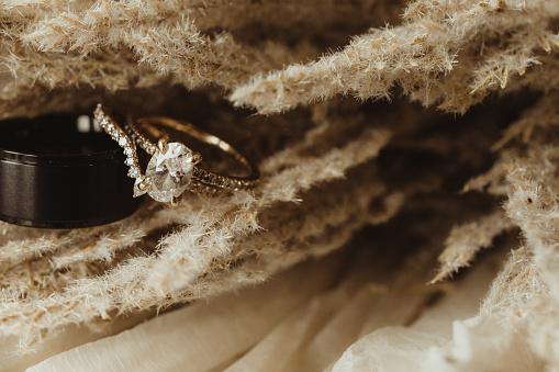 A close-up shot of two gold wedding rings resting on a white pillow with a soft focus background