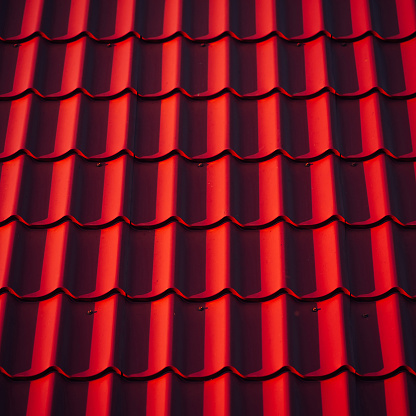 Full frame of vivid red roof covering of undulate shape. Simple texture of steel sloping roof in sunny day. Minimal background of red roofing close-up. Minimalist backdrop of metal roof cover close up