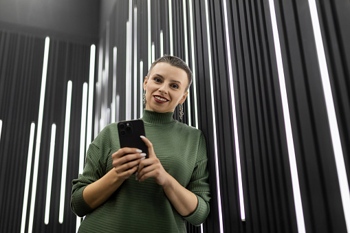 woman with mobile phone near black wall with vertical led lamps.