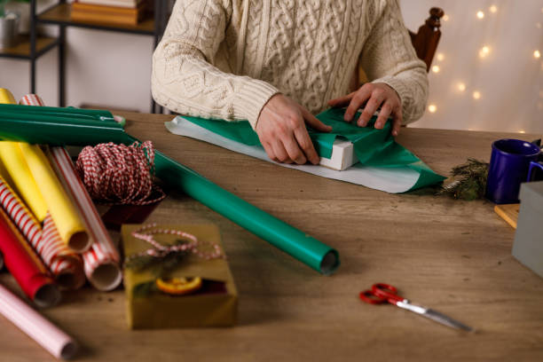 istock Neat young man wrapping a small gift box in green colored wrapping paper 1490833342
