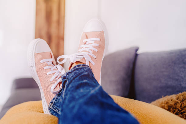 Woman's feet lying on pilow at home.Woman's feet up on the coach, freelancer concept.Copy space.Rest for tired legs of a woman's step.Relaxing Teenager's feet new sneakers on cozy comfortable living room sofa. Relaxing concept on a relaxing day. los pies de la mujer acostados sobre la almohada en casa. pies de mujer en el coach, concepto freelance. espacio de copia. descanse para las piernas cansadas del paso de una mujer. relajante pies de adolescente zapatillas nuevas en el acogedor y cómodo so