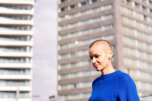 confident woman with shaved head strolling city streets, concept of urban lifestyle and rebel style, copy space for text