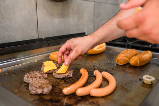 Action shot of male hands cooking. Close up of male chef grilling meat burgers, hot dogs and cheese.