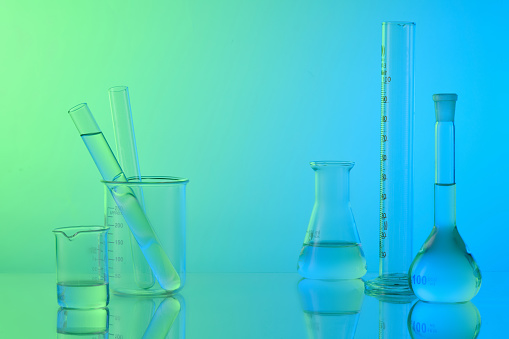 Laboratory concept with lab glassware - erlenmeyer flask, test tubes and beaker filled colorless liquid on gradient background. Space for display product. Minimal style.