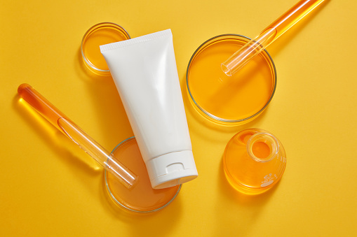 Petri dishes, test tubes and an erlenmeyer flask of orange liquid displayed with a white tube. Minimalism brand packaging mockup. Laboratory experience and research
