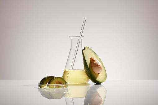 Lab glassware containing essential oil and fresh avocado slice decorated on white background. Avocados are a fruit packed with carbohydrates and healthy fats that provide health benefits.