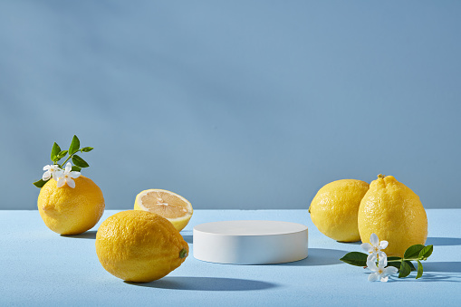 Minimal scene of a white podium in round shape decorated with several Lemons and small white flowers with front view. Light blue background. Organic product promotion of Lemon (Citrus limon) extract