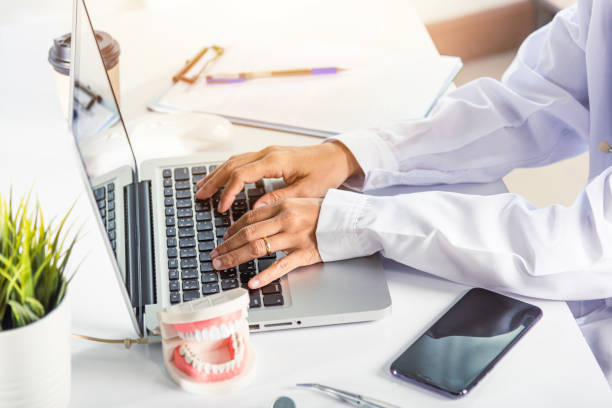 Dentista medico o infermiere in uniforme utilizzare i denti del software orale Raggi X e digitazione delle informazioni modulo di storia medica nel computer portatile - foto stock