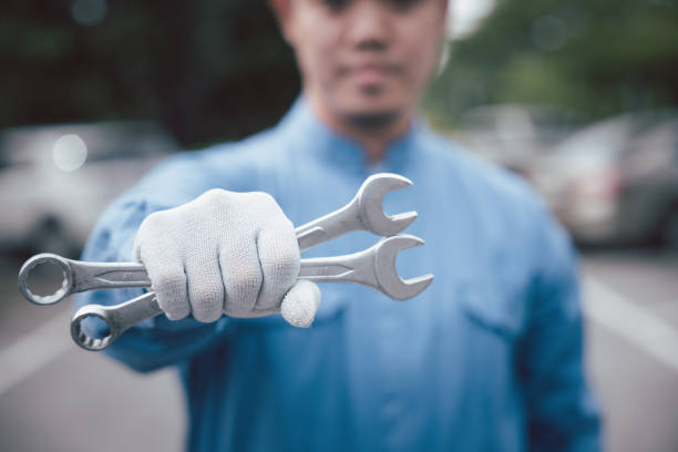 Close up of Man mechanic holding wrench. Skilled car mechanic at work, wearing a blue uniform and holding a large wrench while repairing a vehicle on the road. Close-up shot of hands. in pride we trust stock pictures, royalty-free photos & images