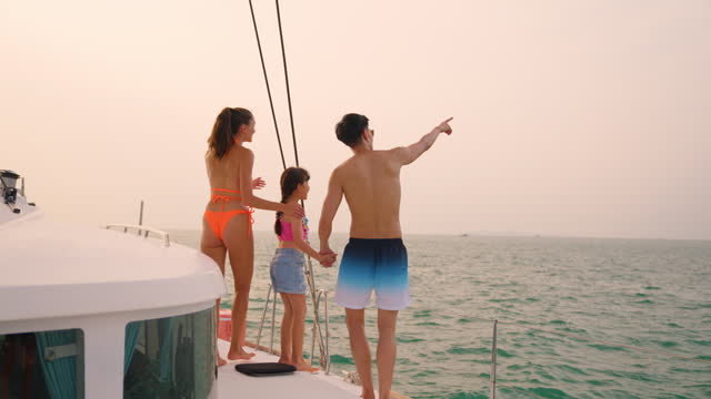 Caucasian happy family walking on deck of yacht while yachting outdoor. Young beautiful couple hanging out and spend time with daughter while catamaran boat sailing during holiday summer trip together
