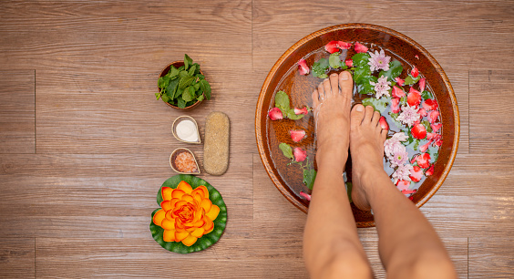 Woman soaks her feet in a bowl with rose flower petals. Foot Spa Concept