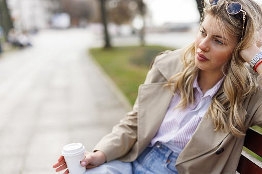 Young woman drinking takeaway coffee while relaxing on park bench